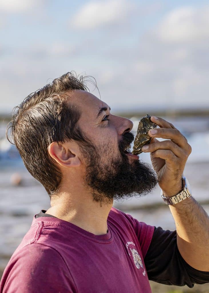 Tom Haward eating a rock oyster on a beach